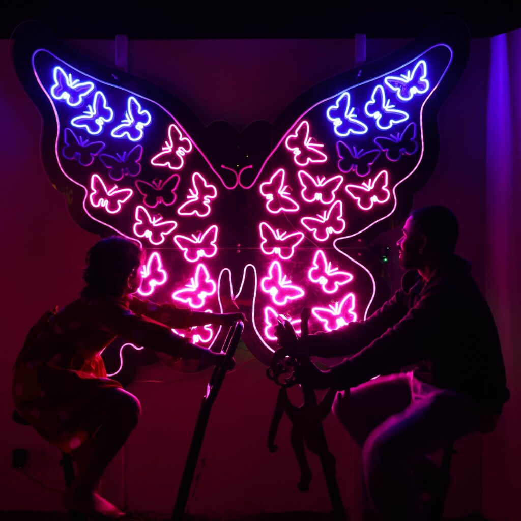 Visitors powering neon butterfly light installation at MAD Labs Bangalore