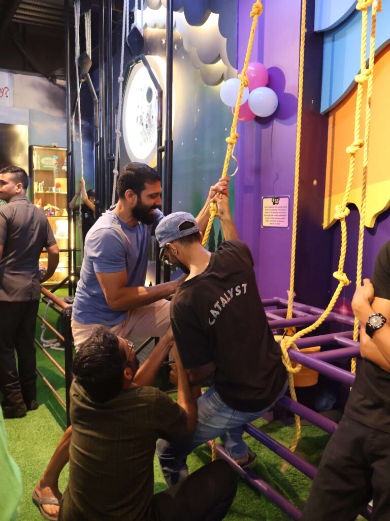 Children attempting a rope climbing activity with moon backdrop at MAD Labs indoor science play zone in Bangalore.