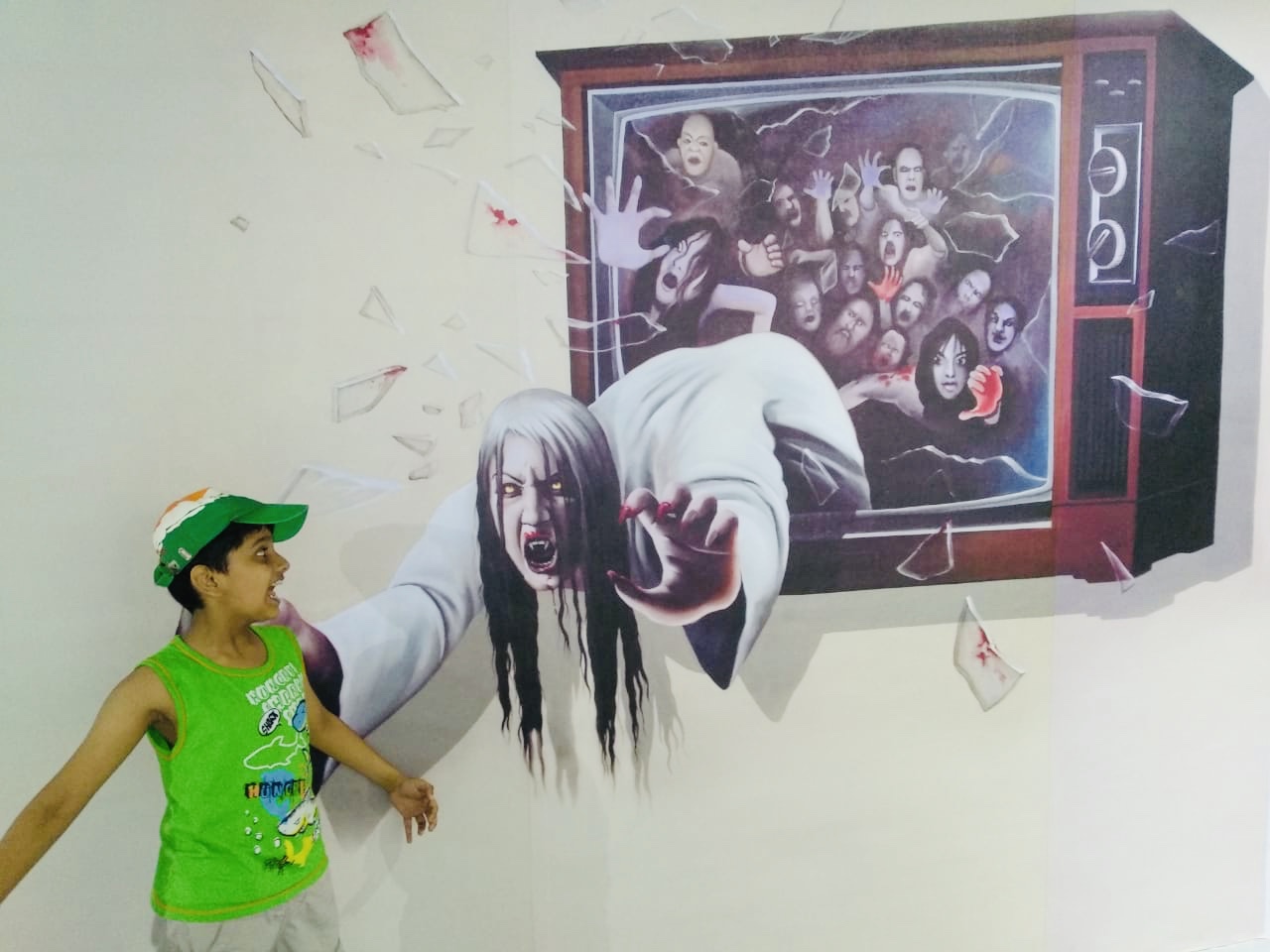 Child posing at Eyelusion Trick-Eye Museum in Snow City Bangalore, interacting with a 3D horror art illusion of a ghost emerging from a TV screen.