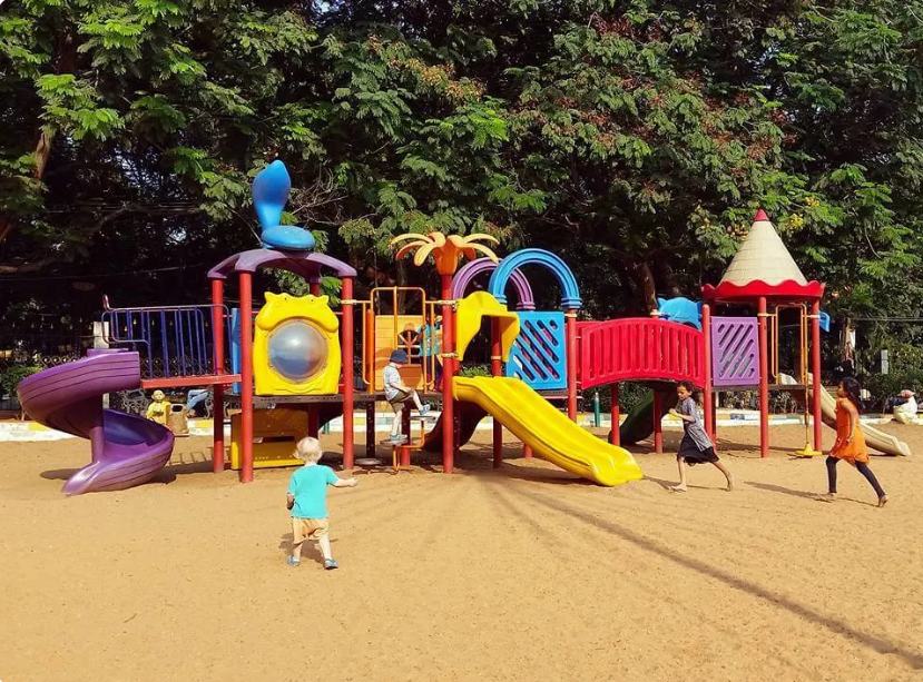 Children playing on colorful slides and climbing structures at an outdoor playground in Bangalore.